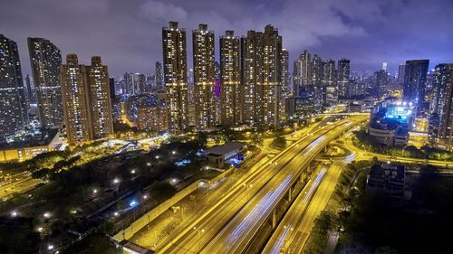 Illuminated road amidst modern buildings against sky at night in city