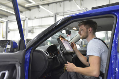 Car mechanic in a workshop using diagnostics computer in car