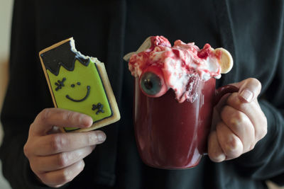 Close-up woman eating halloween cookie and drinking scary beverage