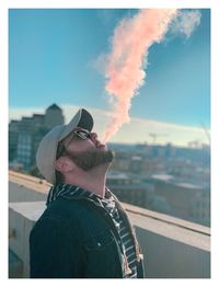 Man emitting smoke while standing against sky