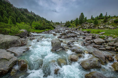 Scenic view of river flowing through rocks against sky