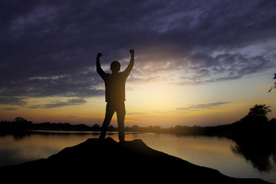 Silhouette man standing by lake against sky during sunset