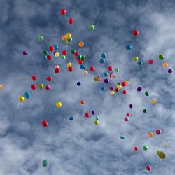 Low angle view of colorful balloons flying against cloudy sky