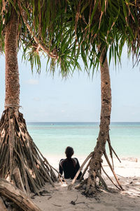 Rear view of woman sitting at beach against sky