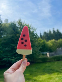 A woman holding an ice cream shaped like a watermelon outdoors in summer season