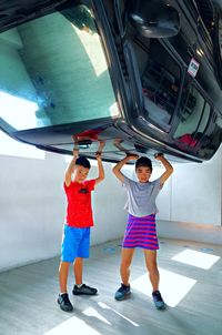 Full length of boy and girl imitating to pick up car while standing on floor