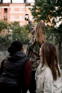 Teenage girl taking selfie with friends through smart phone in city