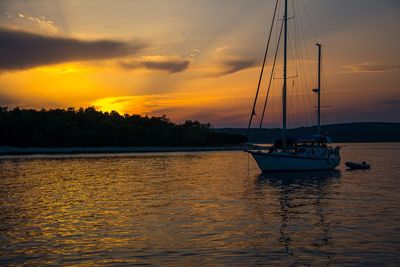 Boats sailing in sea against dramatic sky during sunset