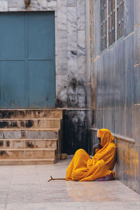 Rear view of man sitting against yellow wall of building