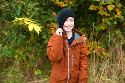 The boy is standing on the street and pulls a hat on his face