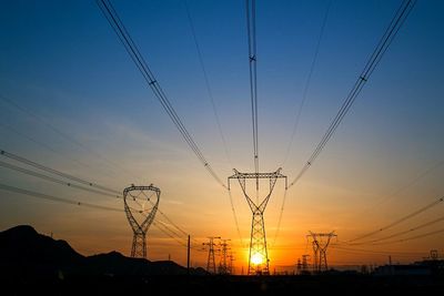 Low angle view of electricity pylons against sunset sky