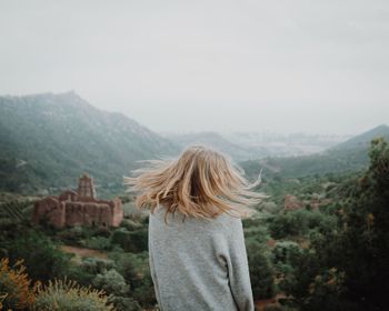 Rear view of woman tossing hair while looking at mountains against sky