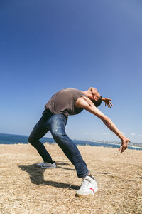 Man dancing on field in front of sea on sunny day