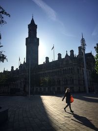 Woman walking on building against sky in city