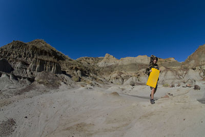 Boy walking on rock against clear blue sky