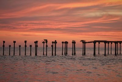 Silhouette wooden posts on beach against sky during sunset