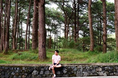 Full length of man sitting on tree trunk in forest