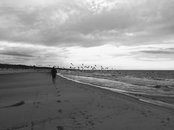 Rear view of silhouette woman walking at beach against cloudy sky