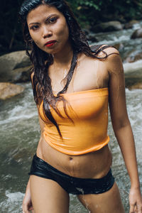 Portrait of young woman standing enjoying in stream at forest