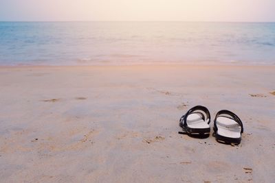 Sandals on sand at beach against sky