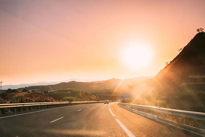 Road by mountains against sky during sunset