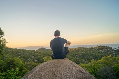 Rear view of man sitting on rock looking at view