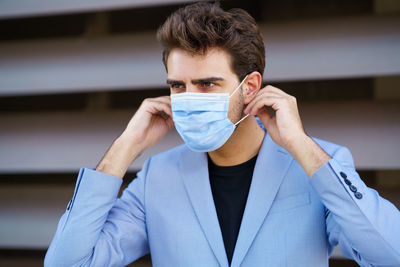 Close-up of young businessman wearing mask looking away while standing outdoors