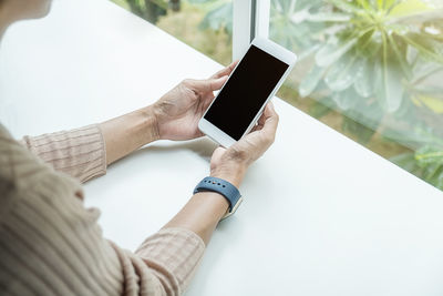 Midsection of woman using mobile phone by window