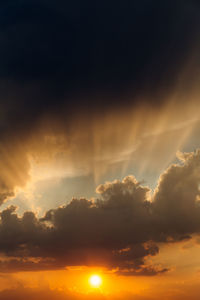 Low angle view of sunlight streaming through clouds during sunset