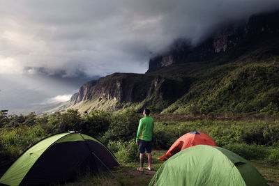 Rear view of man standing at campsite on green mountain