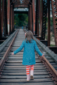 Rear view of girl walking on railroad tracks