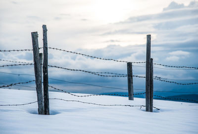 Fence on snow covered field against sky