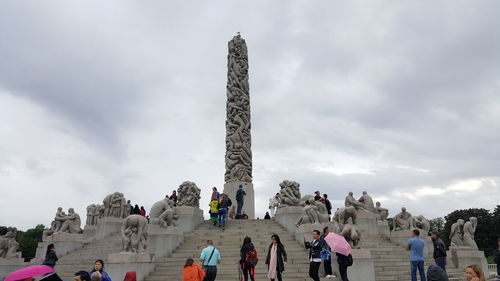 Low angle view of tourists statue against cloudy sky