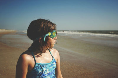 Girl wearing swimming goggles while looking at sea on st. augustine beach during sunny day