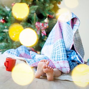 Cute child wearing blanket sitting by illuminated christmas tree