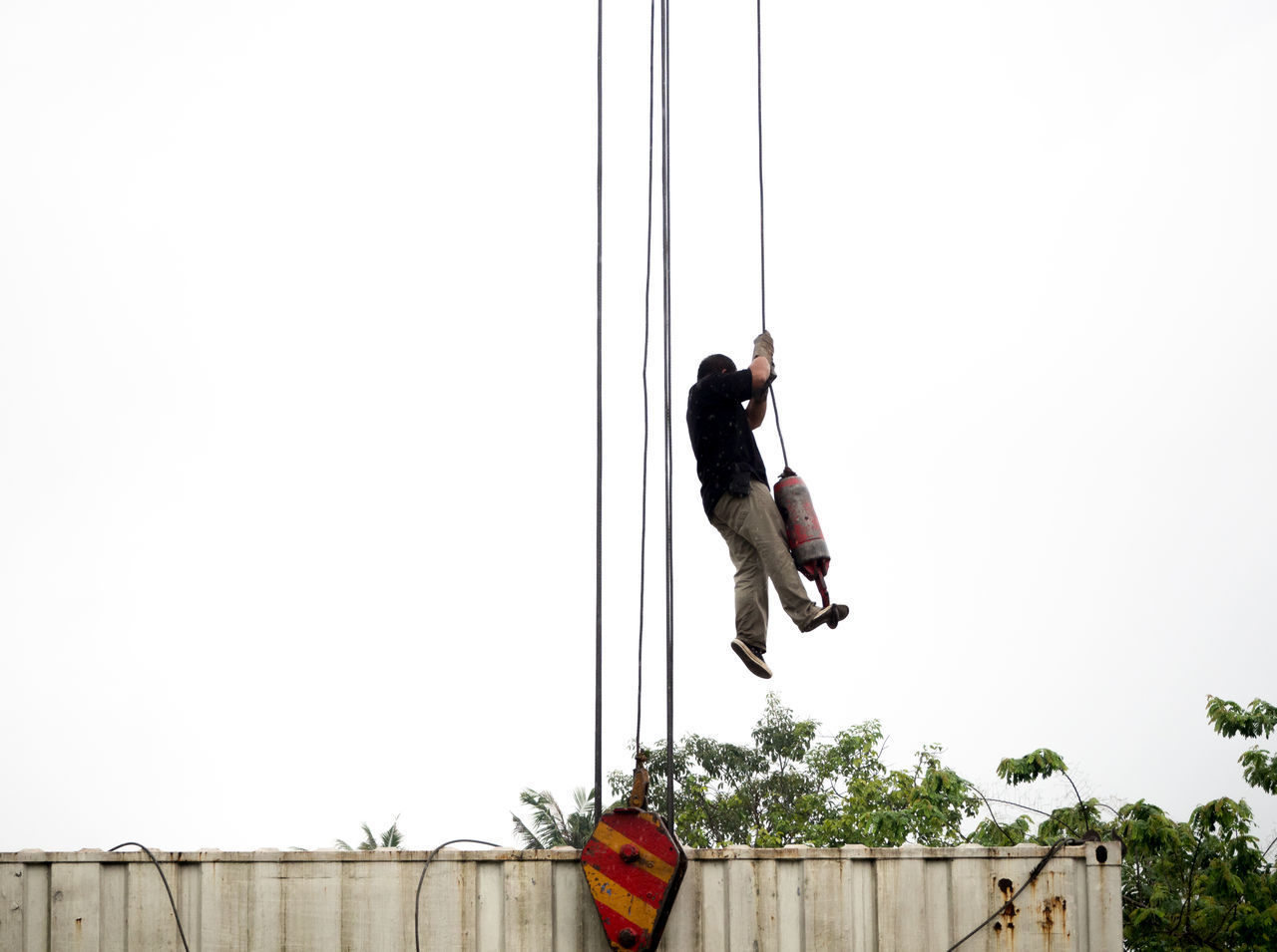 LOW ANGLE VIEW OF MAN HANGING ON ROPE