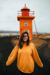 Happy woman standing near orange lighthouse near sea