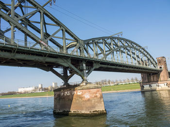 Low angle view of bridge over river against clear blue sky