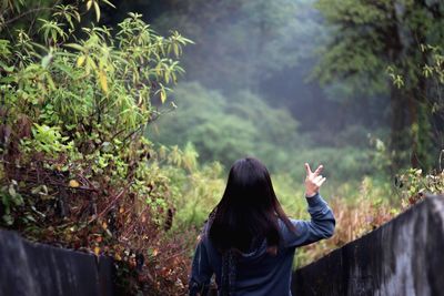 Rear view of woman showing peace sign against trees