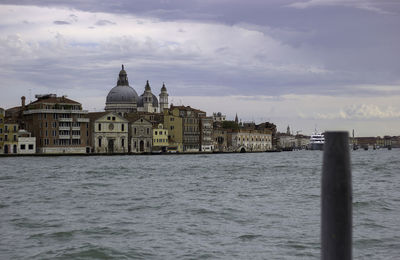 Buildings by river against cloudy sky