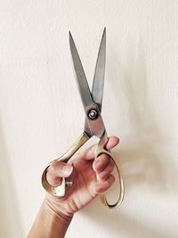 Cropped hand holding golden vintage scissors against wall