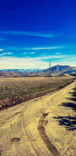 Dirt road amidst field against blue sky