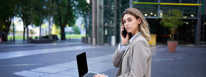 Portrait of young woman using mobile phone in city