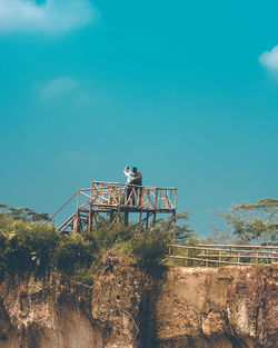 Low angle view of man standing by railing against blue sky