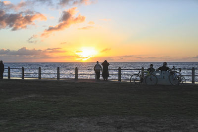 Silhouette people standing on beach against sky during sunset