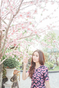 Portrait of woman standing by pink flowers against tree