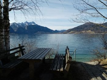 Empty bench by lake against sky