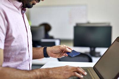 Midsection of businessman with credit card using laptop computer on desk in office