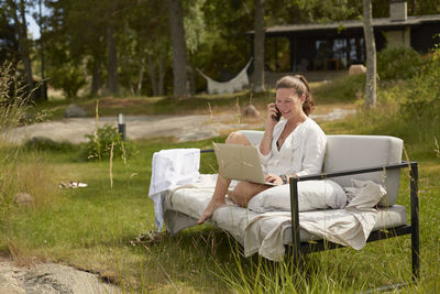 Woman taking via cell phone on garden bench barefoot