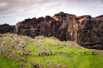 Hikers walking on hill against rocky mountain